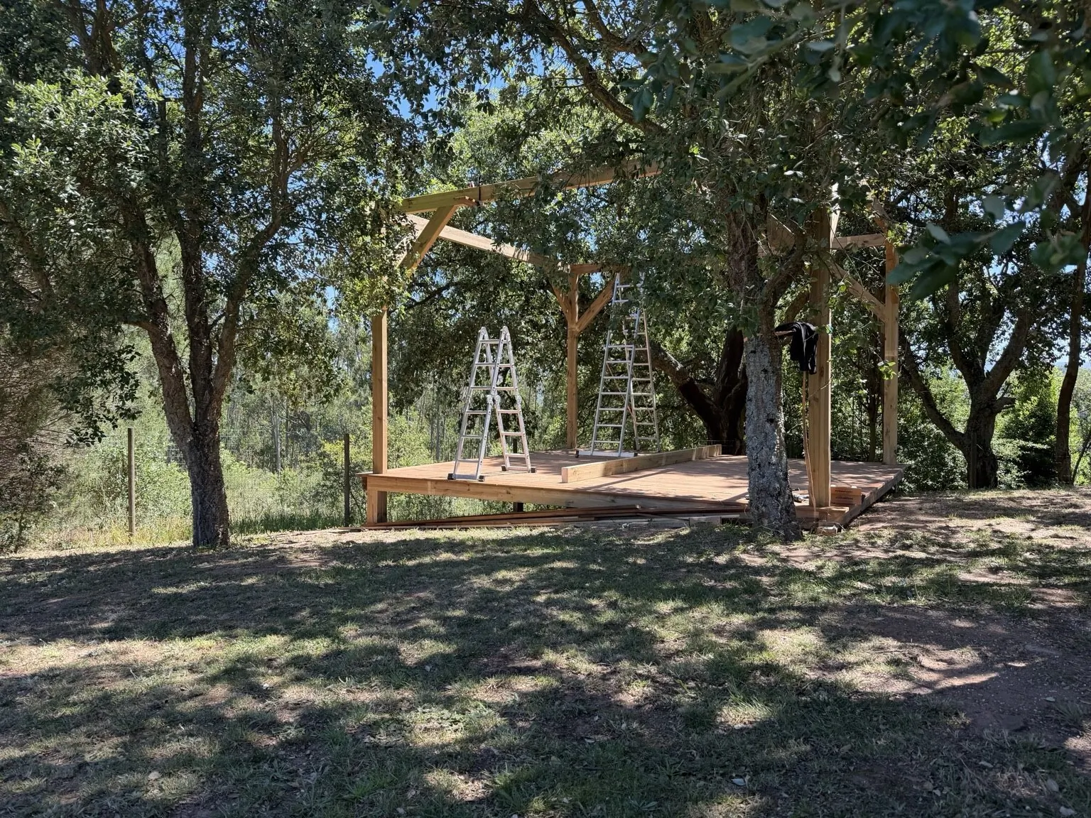 Outdoor gathering platform under construction beneath mature trees